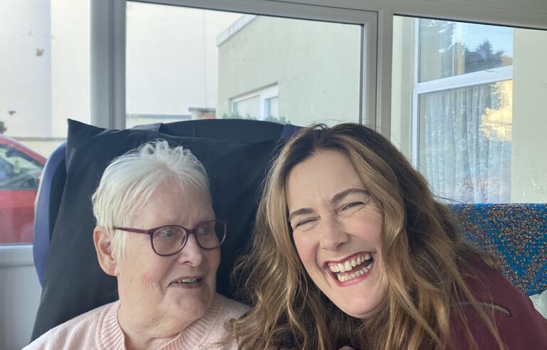 A younger woman crouched next to an older woman sat in a chair