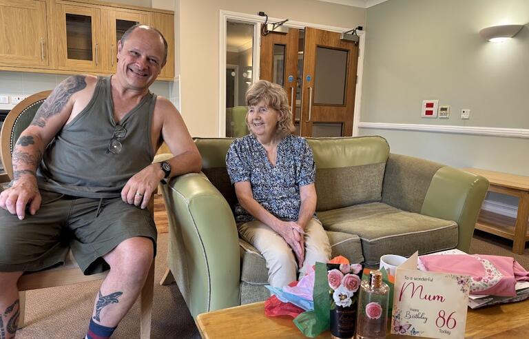 A man sat on a chair next to a woman sat on a green sofa