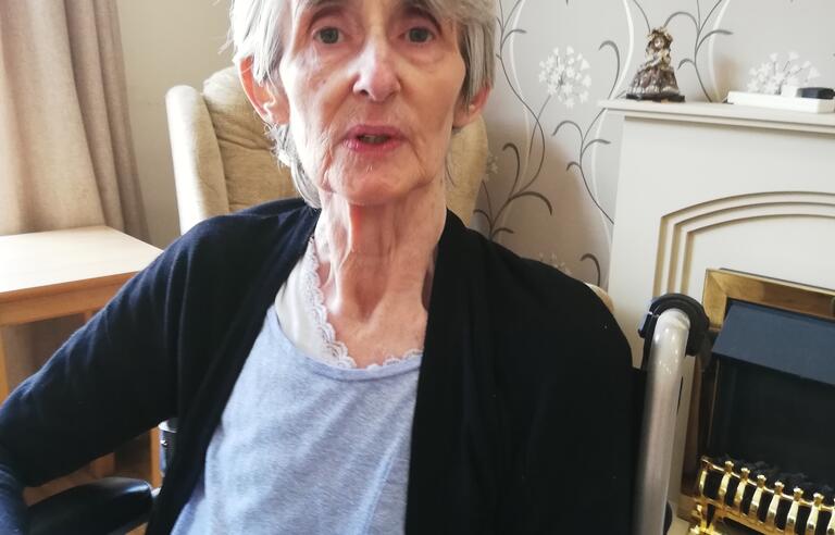 A woman with short grey hair wearing a blue top and black cardigan