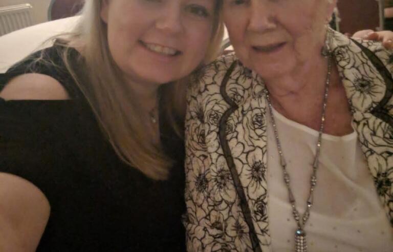 A selfie of a younger woman with blonde hair wearing a black top and an older woman with short white hair, a white top and patterned jacket