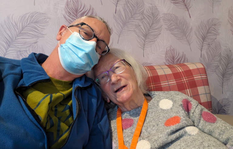 A man wearing a face mask with his head resting on a smiling woman