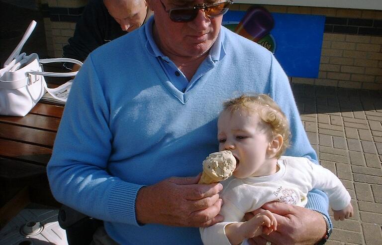 A man holding a baby feeding them an ice cream cone