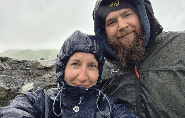Two people taking a selfie on a mountain wearing wet waterproofs