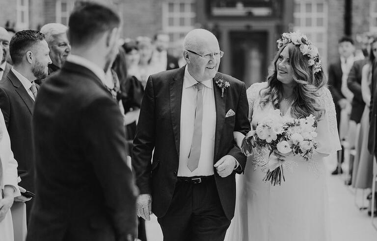 A black and white photo of a man walking a bride down the aisle
