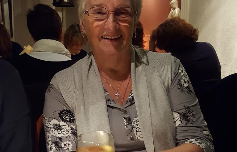 An older woman with short grey hair, and a grey top smiling while holding a glass of wine