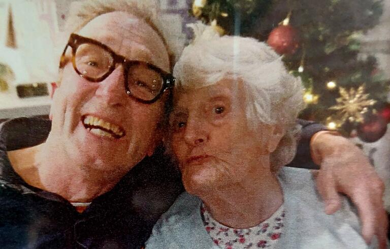 A smiling man hugging an older woman with a Christmas tree in the background
