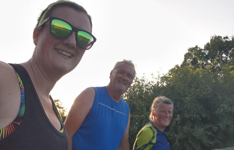 A woman and two men in running clothes with sky and trees behind them