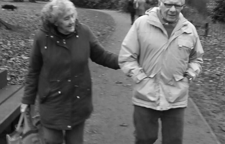 A black and white photo of a woman and man walking in a park