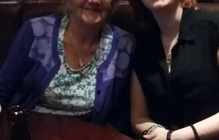 An older later with short grey hair and glasses sat with a younger woman with a ginger bob and glasses. Both are in a pub and smiling