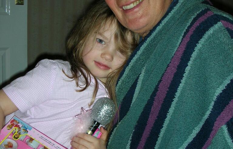 A man with grey hair in a stripy green dressing gown hugging a girl with brown hair and wearing all pink