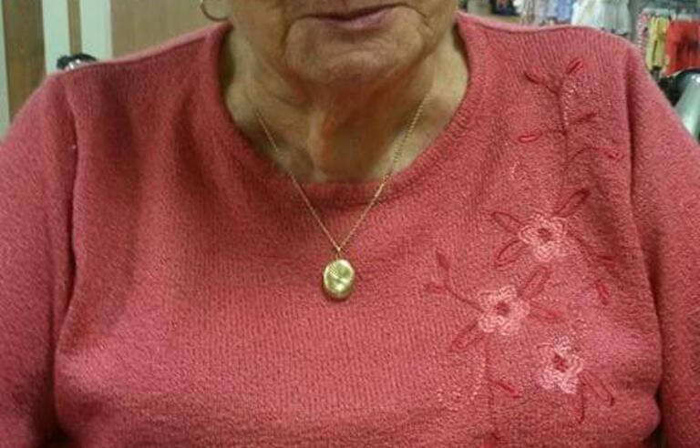 A woman with short, grey curly hair wearing glasses and a pink jumper eating a scone