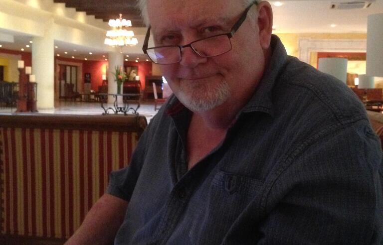 A man with white hair, glasses and a blue shirt holding a phone