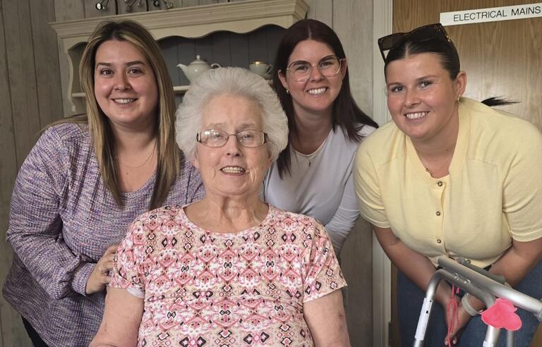 An older woman in the foreground and three younger women stood behind her, all smiling