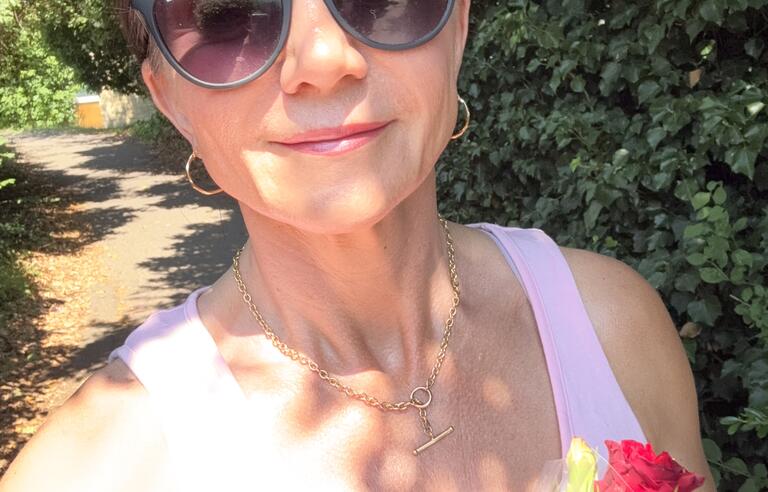 A selfie of a woman wearing sunglasses and holding a bunch of roses