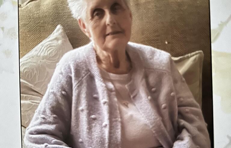 An older woman with short white hair wearing a pink top and cardigan