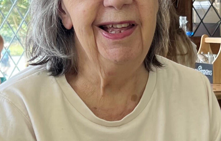 A woman with grey hair, glasses and white top with a glittery motif