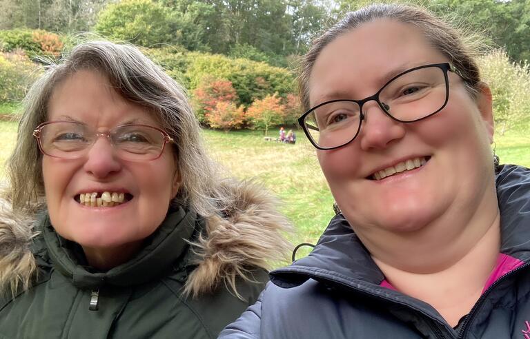 A woman with blonde hair and glasses wearing a green coat and a woman with blonde hair and glasses wearing a blue coat