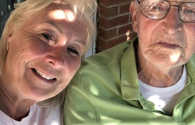 A woman with short blonde hair smiling next to an older bald man wearing glasses and a green t shirt