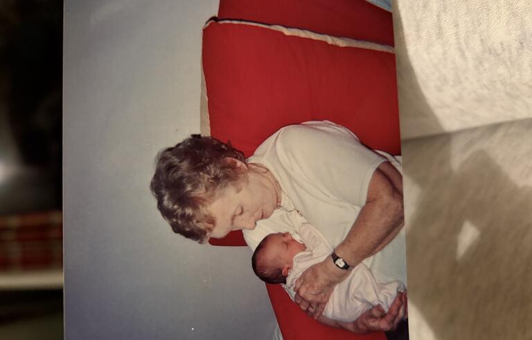 A woman sat on a red chair with short curly blonde hair and a white t shirt cuddling a newborn