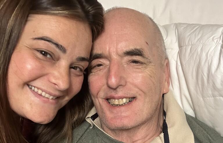 A smiling woman and man, who is resting on two white pillows