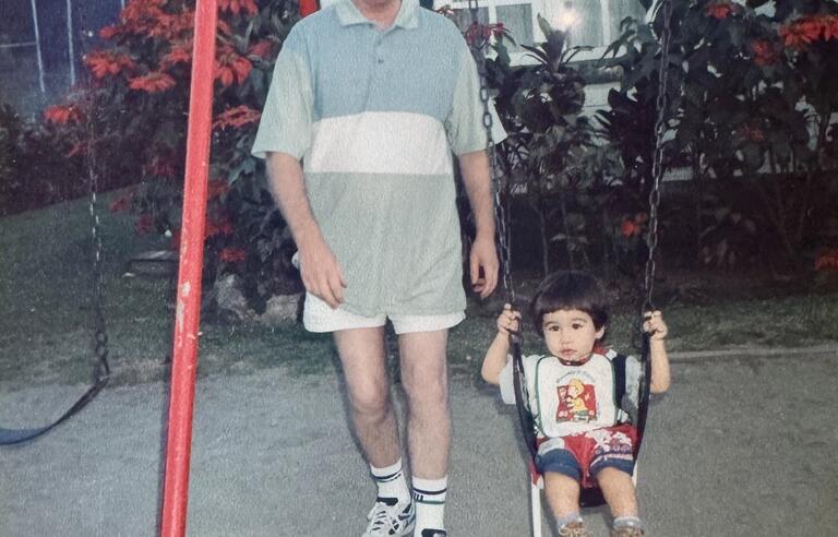 A man stood next to a toddler on a swing