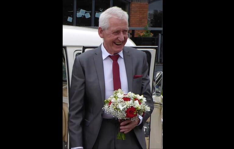 A man in a grey suit with a red tie holding a bouquet of flowers 