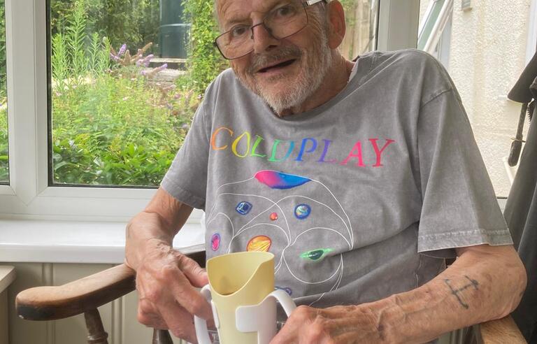 A man holding a cup and smiling sat in a wooden chair